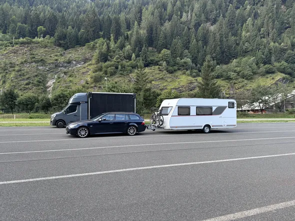 Car towing a caravan with bicycles on the Brenner Autobahn in Austria, with truck and forested Alpine mountains in the background